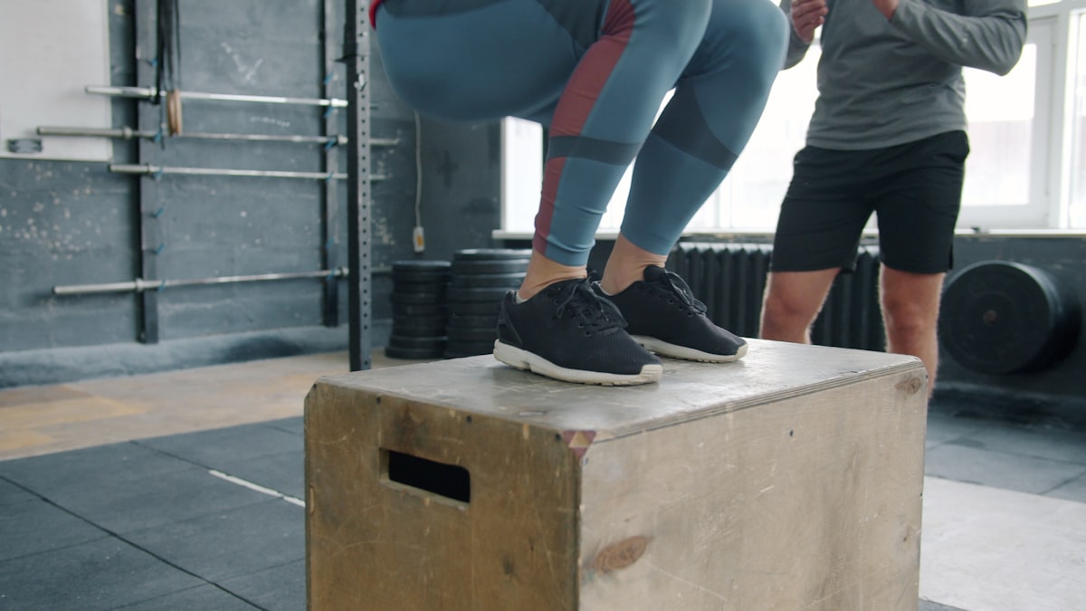 Young athlete performing a box jump with a coach
